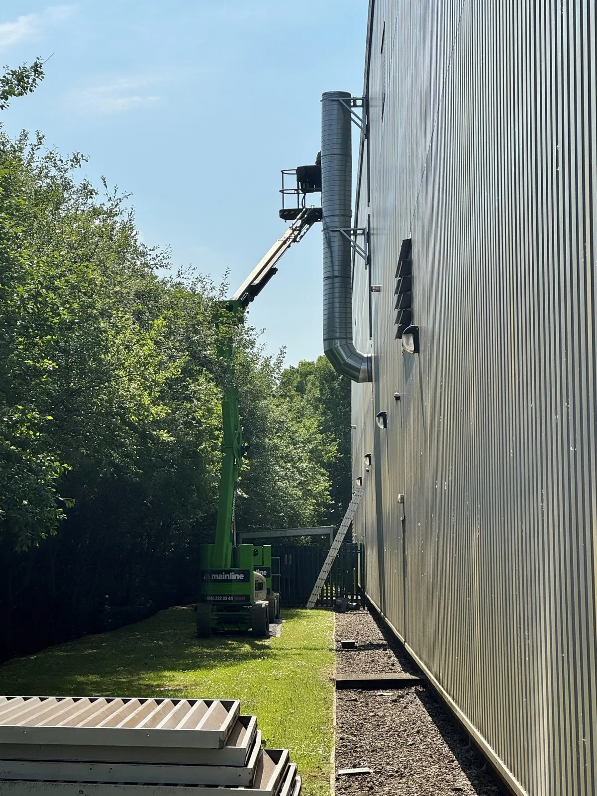 Boom lift positioned beside external ducting on the side elevation of the building