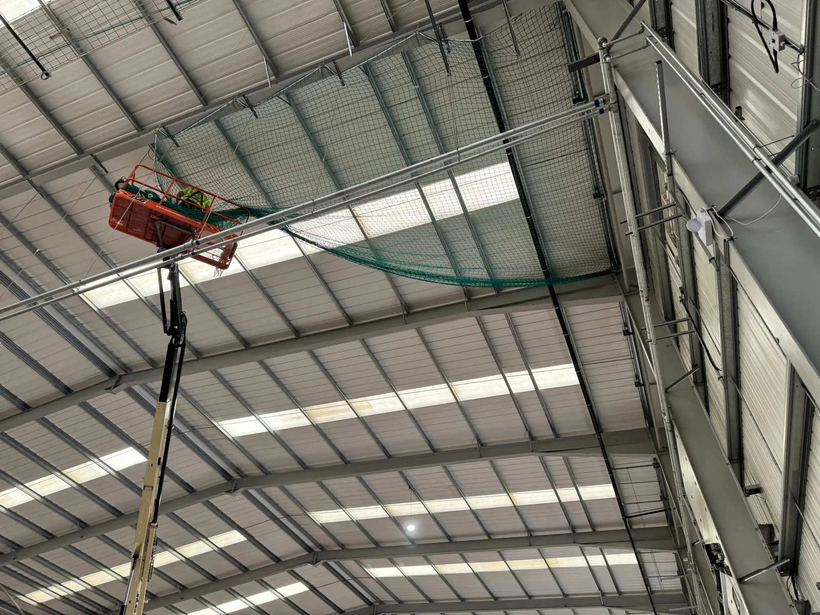 Safety netting rigged at roof level inside the hall with an operative in a boom lift basket